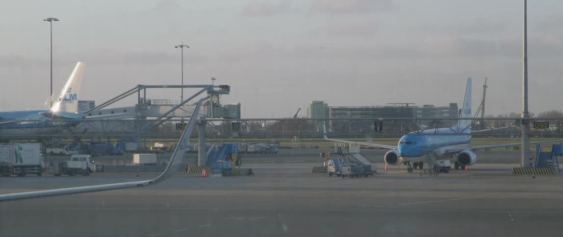 Airplanes taxi down a runway while ground crew vehicles transport large containers