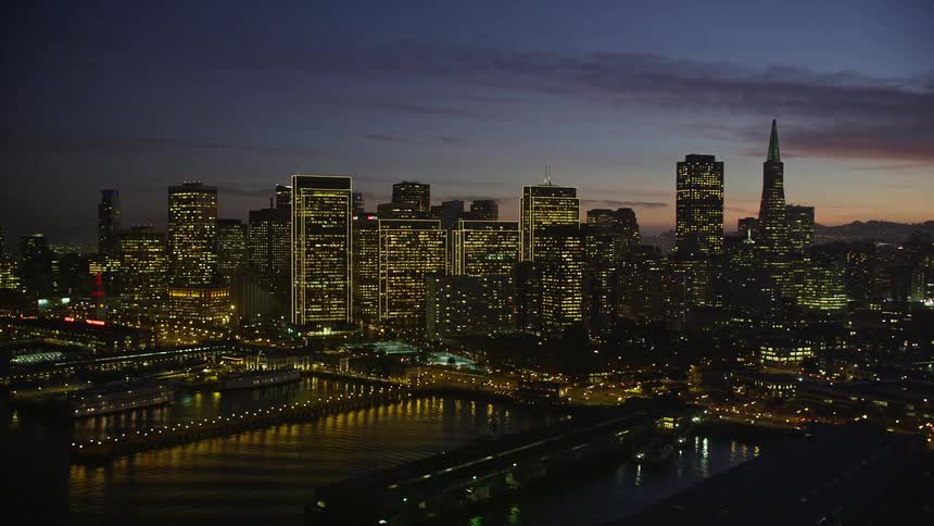 Brightly lit skyscrapers of coastal city contrast with red horizon