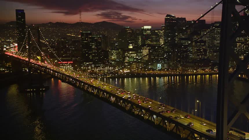 Numerous vehicles are traveling across a suspension bridge leading to a large city