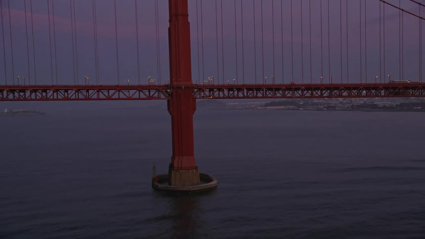 Traffic crosses suspension bridge across the water from foggy coastal city