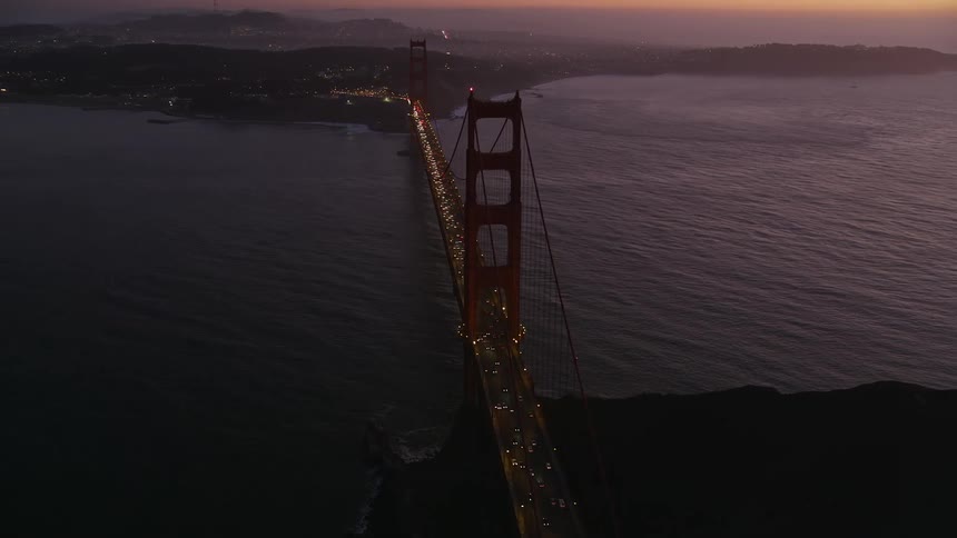 A suspension bridge over the sea with a highway above with many cars passing by and with their headlights on