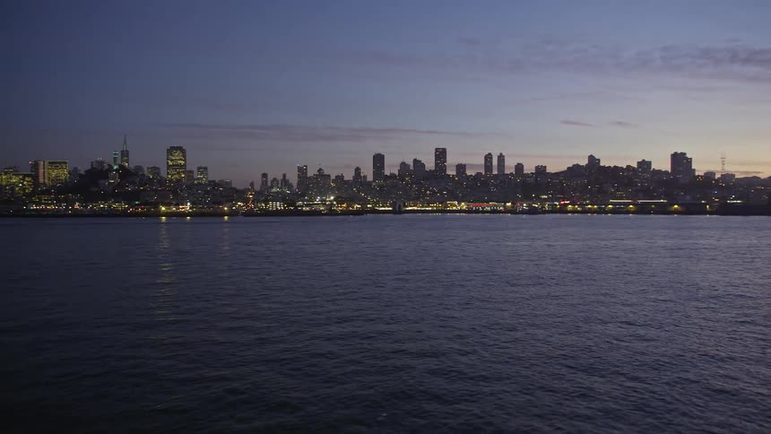 Aerial aerial panorama of a calm ocean and in the background a metropolis illuminated in the evening of a purple sky