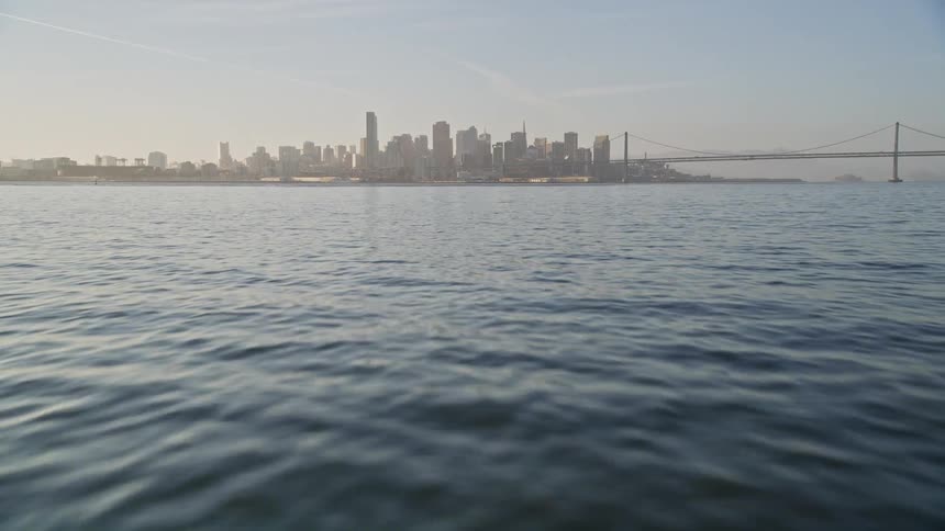 Moving over the water with a metropolitan city skyline and bridge in the distance