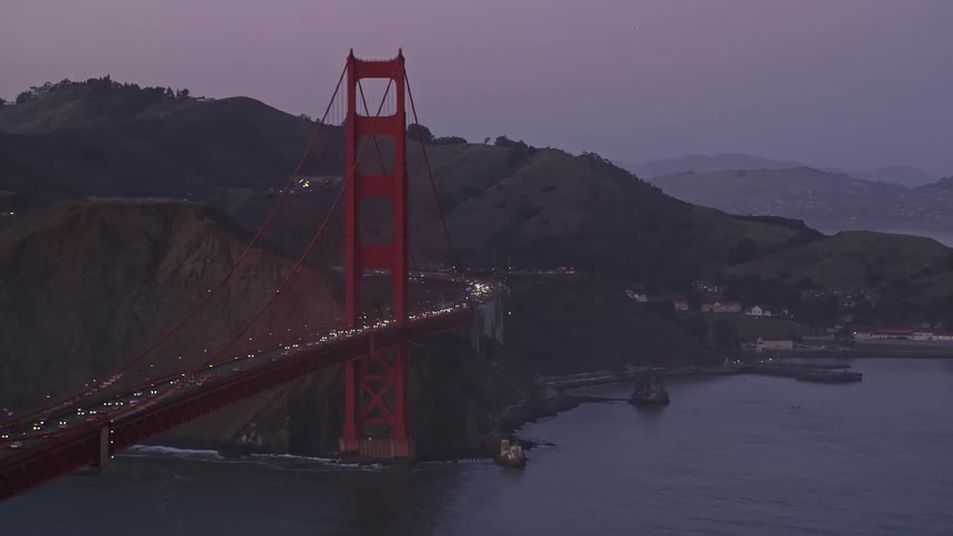 The golden gate bridge illuminated in orange stretches across the dark blue waters of the san francisco bay at night