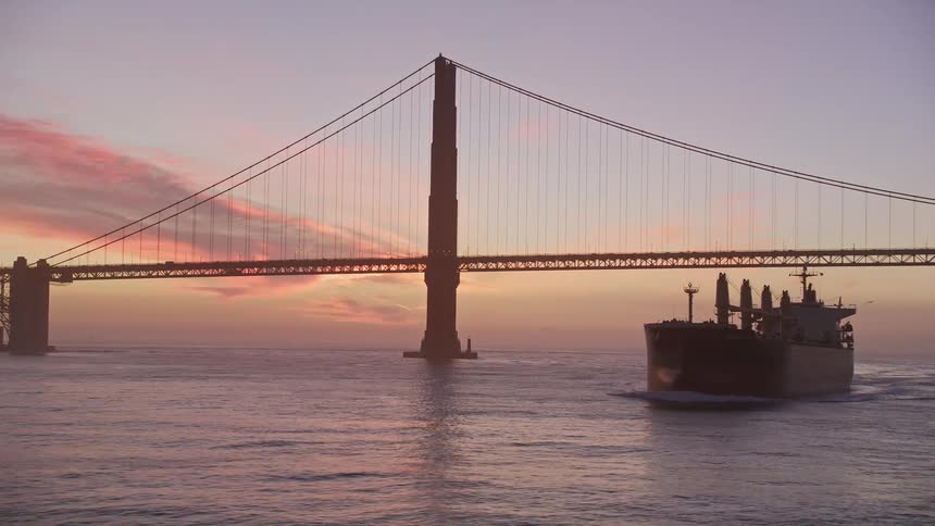 Freighter passes under suspension bridge silhouetted against the red tinted sky