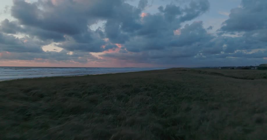 Moving over a field along the coast as waves roll into shore under a cloudy sky