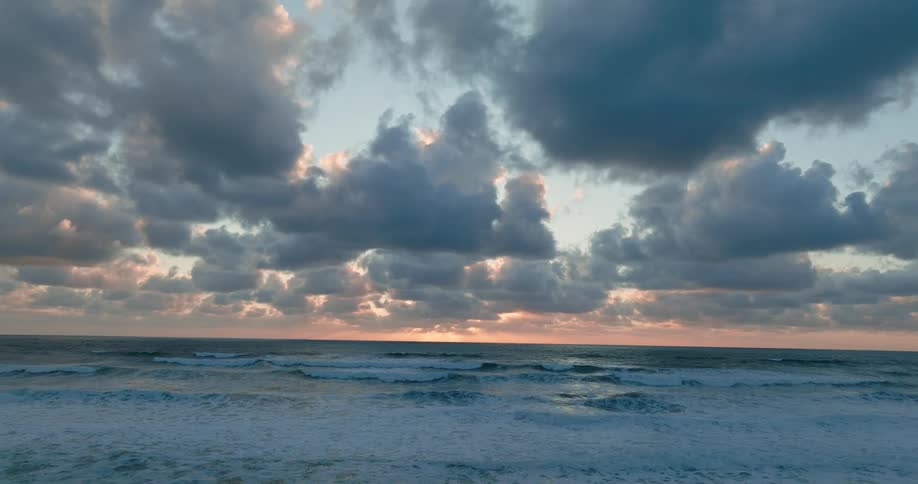Waves foam while rolling onto beach at sunrise on a cloudy day