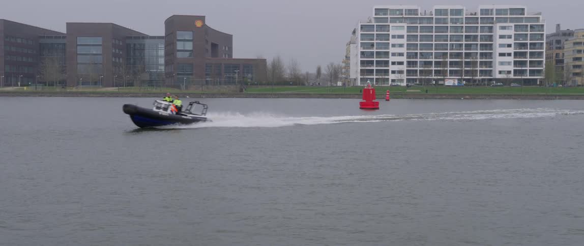 A boat with two people moving across calm water near a red buoy