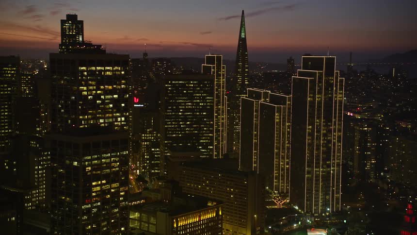 Building lights illuminate coastal city against a red tinted horizon