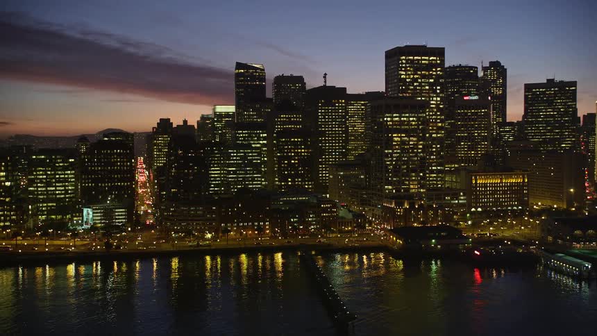 Modern urban and commercial cell buildings by the sea illuminated at dusk against a purple and reddish sky