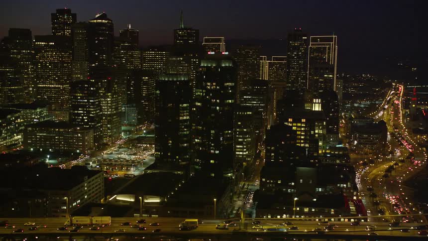 Aerial panorama of urban and commercial buildings seen at night with a bridge with vehicle traffic in front