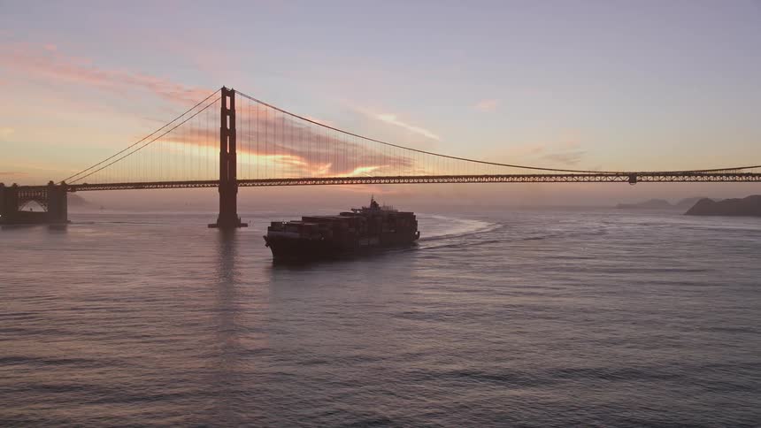 Aerial view of a cargo ship passing through a sea canal with a bridge on a red sky day