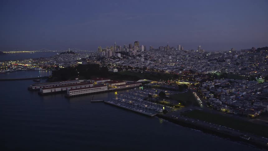 Aerial panorama with a metropolis illuminated at dusk at night by the sea and with the purple sky