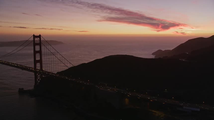 Heavy traffic crosses the golden gate bridge as sunlight tints the horizon red during sunrise