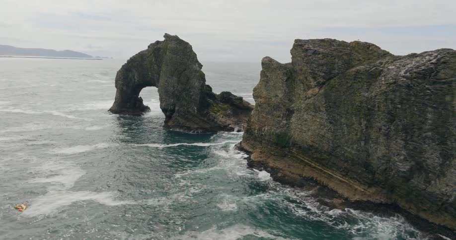 Waves splash against rock formations and an arch along the coast