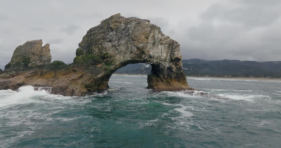 A rocky arch formation with ocean waves and a cloudy sky