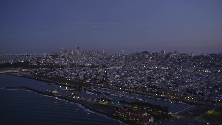 Traffic flows along waterfront highway passing a marina and a domed building far from the downtown skyline at night