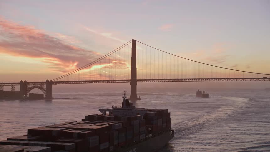 Panorama of a cargo ship with containers and the golden gate bridge in the background against a red sky