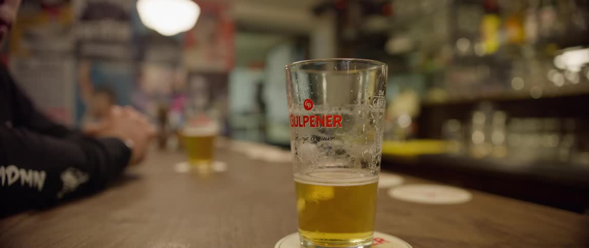 A hand picks up a beer glass from a bar