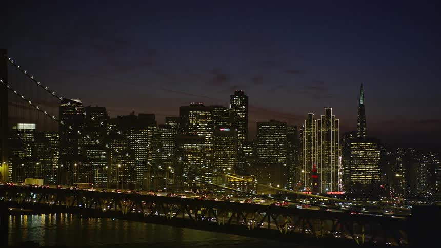 Aerial scene of an extensive bridge with vehicles traveling and in the background a metropolis illuminated at night