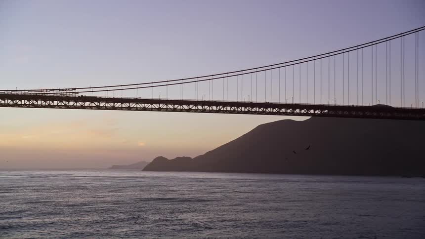 Aerial view of a freight ship near a suspension bridge at sunset
