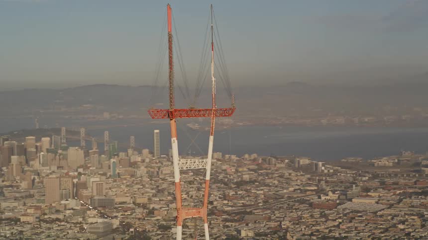 Aerial view of an orange and white signal transmission tower and in the background a metropolis by the sea
