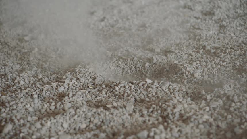 A bullet hits the ground kicking a small cloud of white dust