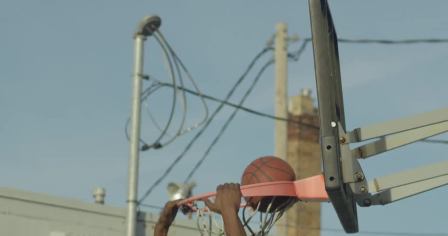 A black man stuffs a basketball through the net