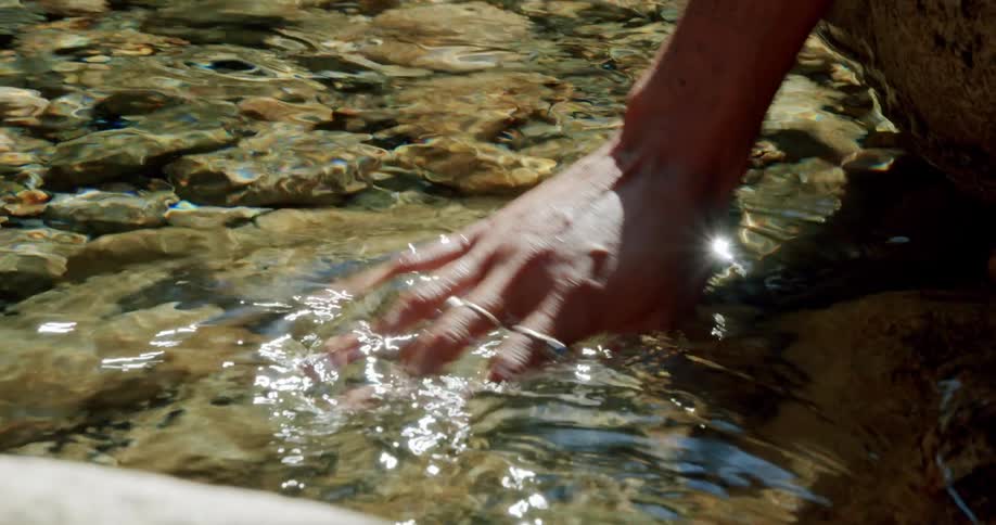 A person playing with clear water from a rocky stream