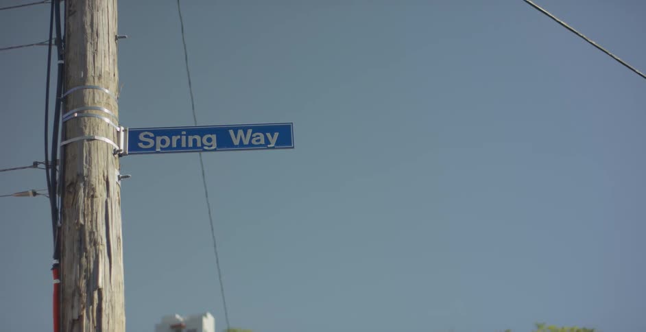A blue sign with white writing hanging from a lamppost in contrast to the blue sky