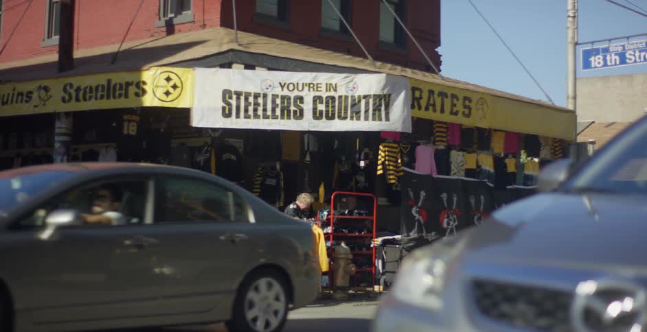 A storefront with a white banner on top with writing in black and in front there are several cars passing on the street