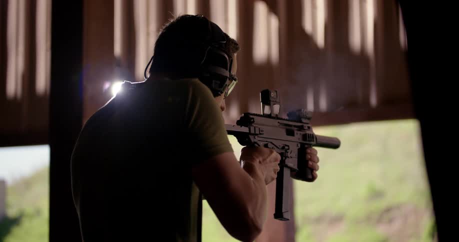Man with protective glasses and a noise headset reloading and shooting a gun in a training center