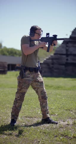Man concentrated in an open field using glasses and antinoise headphones shooting with a military weapon