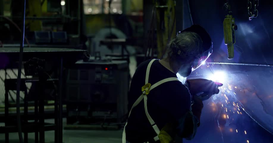 A person wearing safety gear in a workshop welding a large metal structure with sparks flying