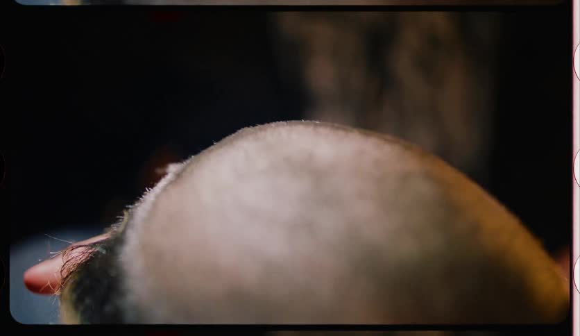 A barber shaving and styling the hair of a balding person