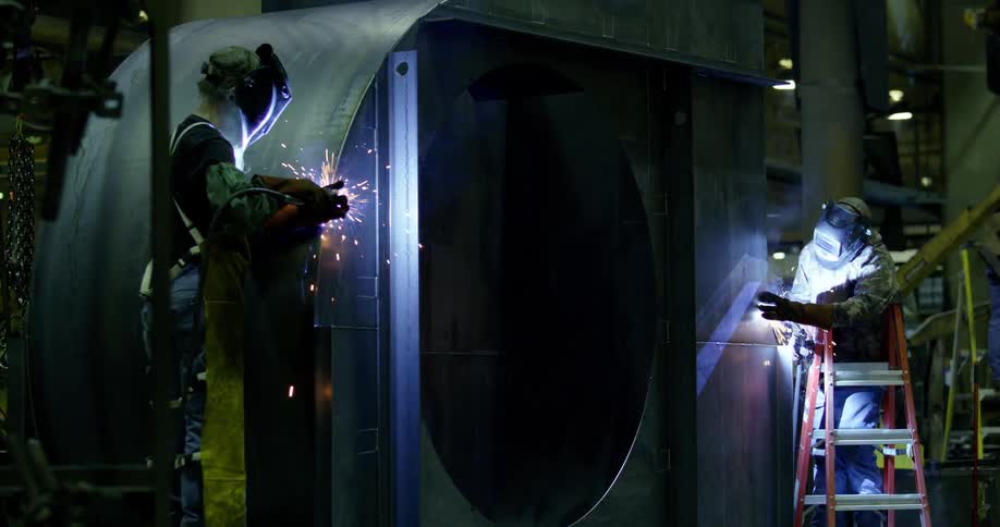 Two metalworkers are welding a large metal structure in a factory
