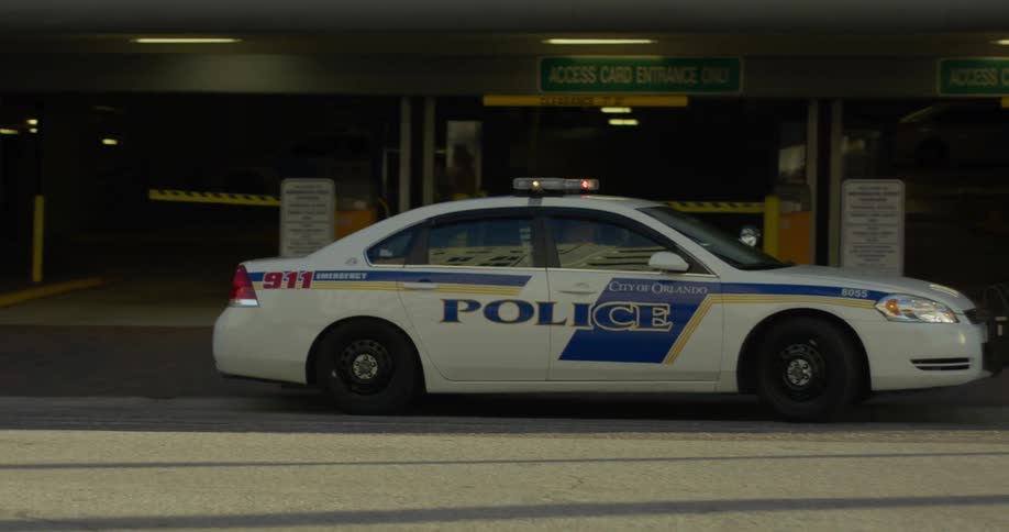 Police car with flashing lights pulls away from urban building and onto city street