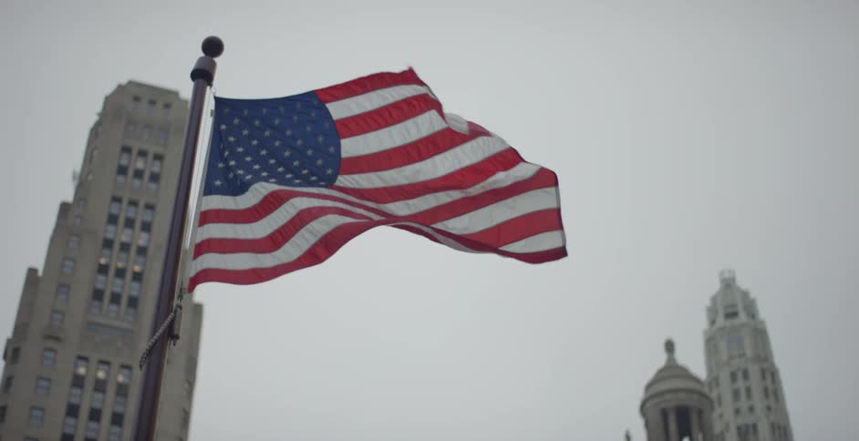 A flag blowing in front of tall buildings in a city