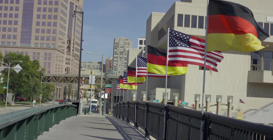 A downtown urban city street has flags attached to a bridge railing