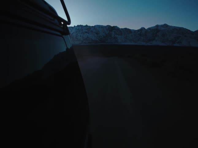 A vehicle drives across flat terrain near mountains
