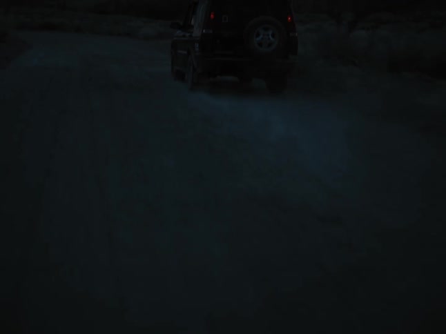 A vehicle driving along a dirt road with a mountain range in the distance