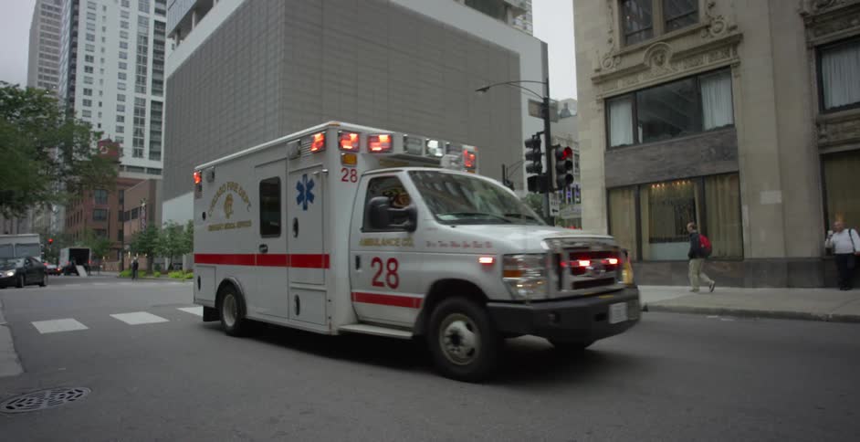 An ambulance and a yellow taxi are at an intersection in a city