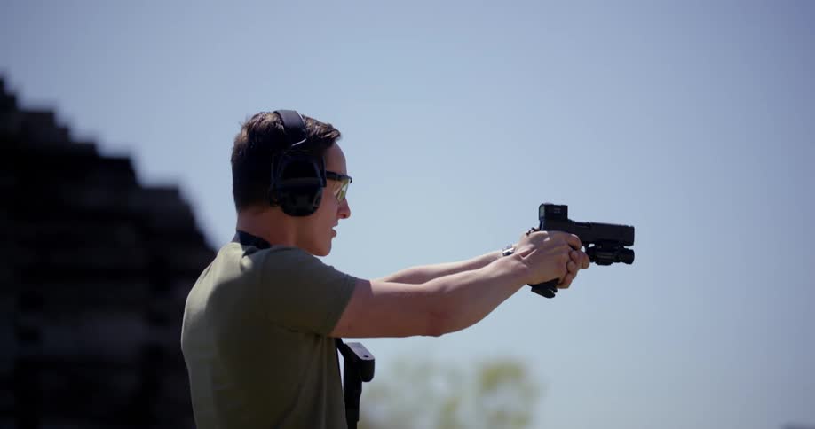 Man shoots and reloads a handgun in front of a forest