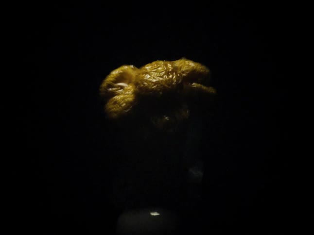 Dense object of golden color compressing in an abstract way and submerged in a dark background