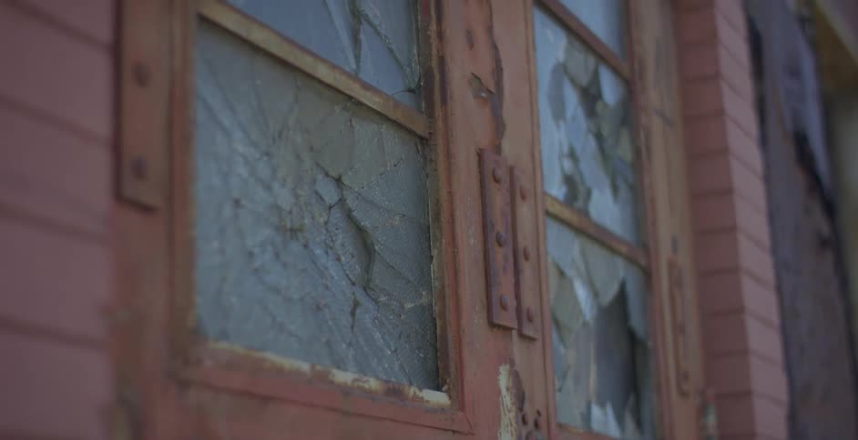 A closeup of a broken window with shattered glass and wooden frames