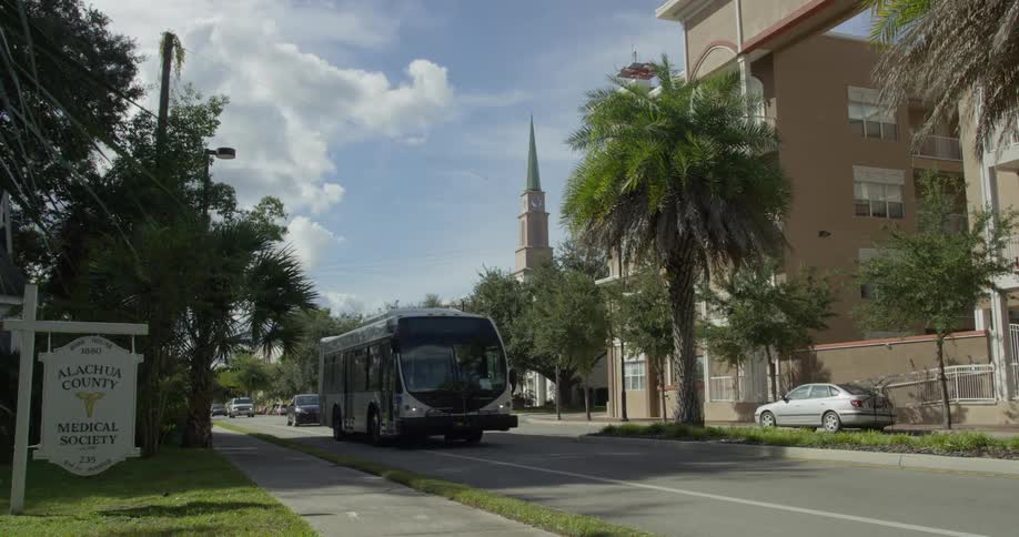 A street view with a sign on the left and a church steeple in the background on a sunny day