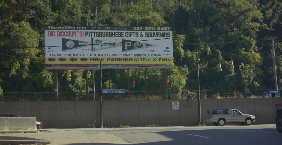 Various cars drive by a billboard promoting a company selling sports memorabilia