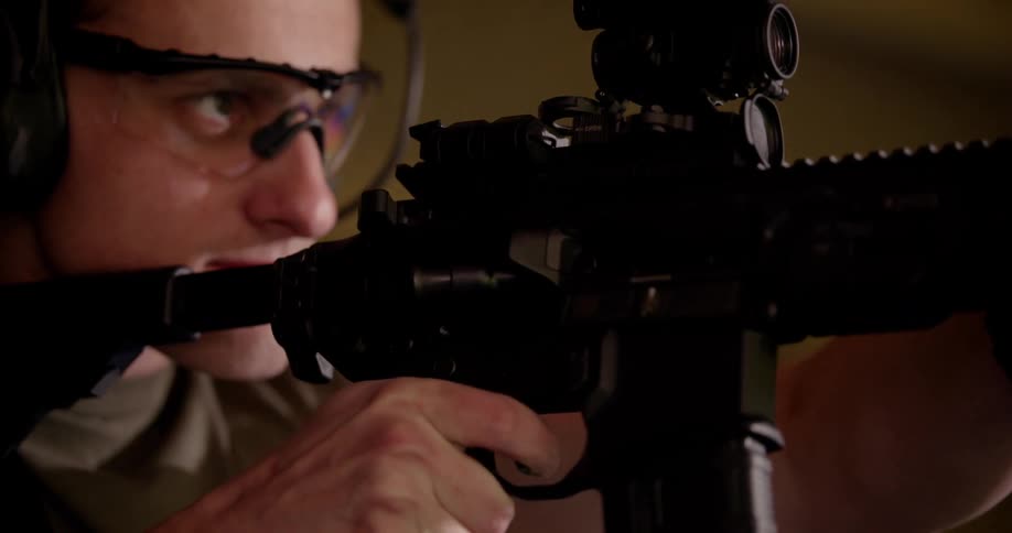 A men wearing goggles is aiming with a black rifle and shooting and several bullet casings are coming out