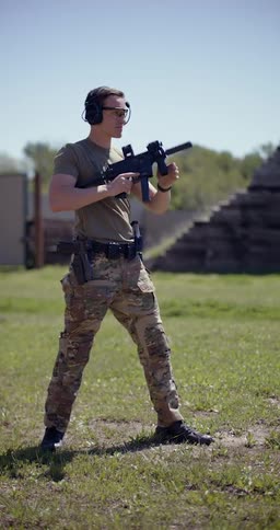 A person standing outside at a firing range holding a firearm aiming and shooting