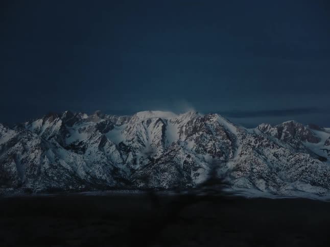 A dark sky over a snowcovered mountain range seen from a moving vehicle